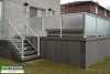 Grey composite deck with frosted glass railing attached to a grey brick house.